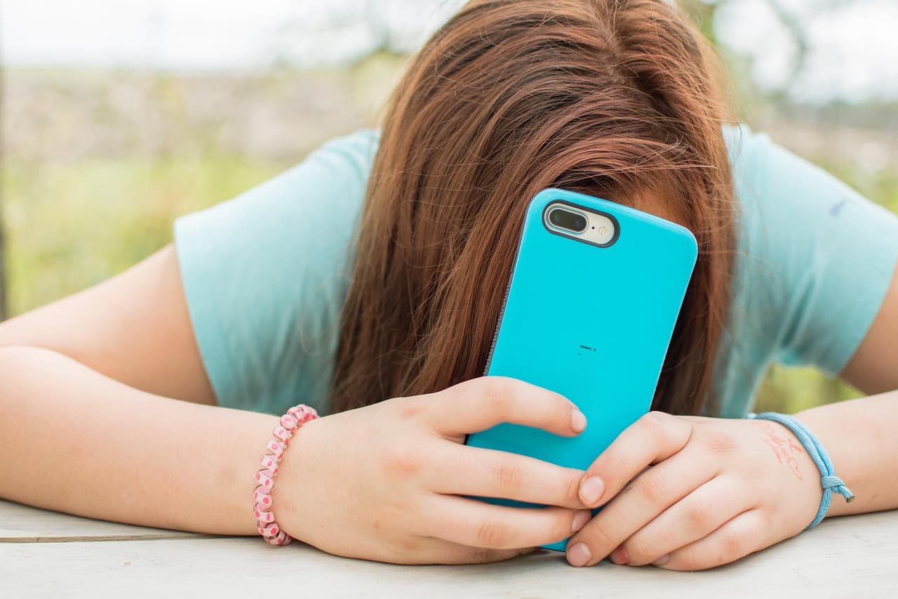 A teenage girl with her head down, hiding behind her phone